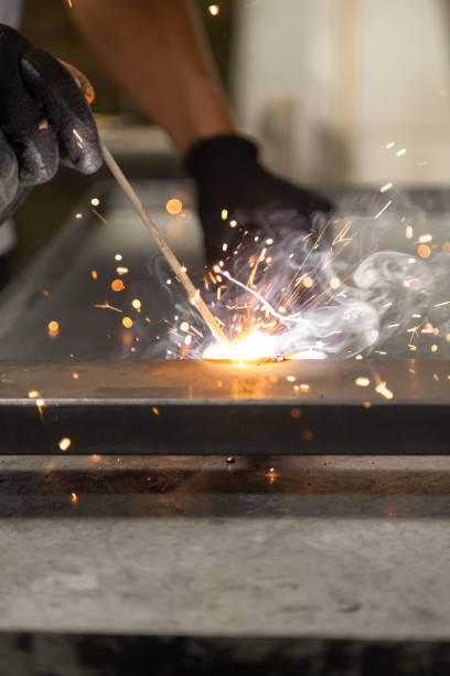 istock person's hand wearing protective gloves while using a metal welding tool, sparks from the machine, manual work 1345893839