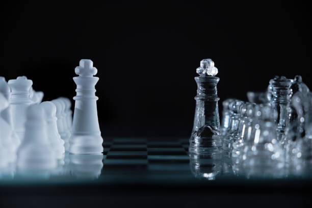 istock glass chess kings facing each other on a glass board on a black background with copy space 1345896100