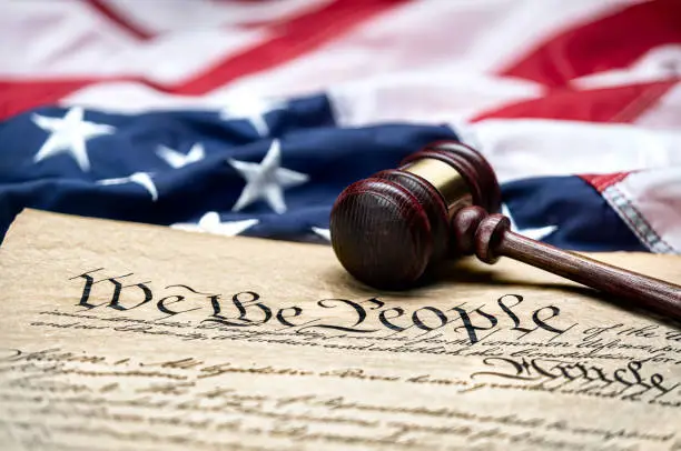 American flag draped around a judge's gavel block and the United States Constitution for use as a symbol of laws, freedom and separation of government powers.