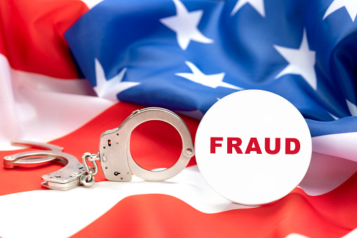 Images depicts a fraud button against handcuffs and the American flag, insinuating that fraud is a crime and those cheating people will be arrested.