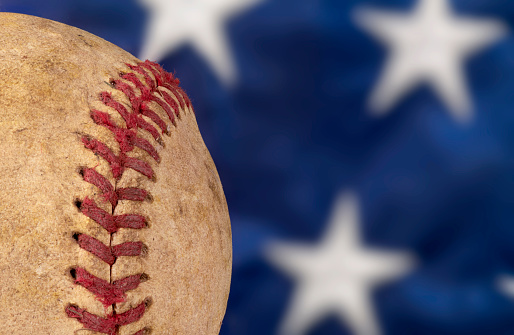 Close up of an old, used baseball against an American flag highlighting the national pastime of the United States.