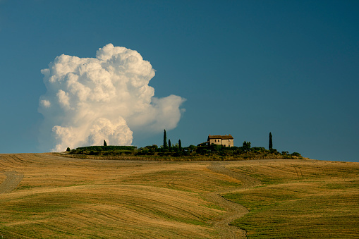 Tuscany, Italy - August 12, 2018: Unique cumulus cloud formation over a farmhouse in Val d