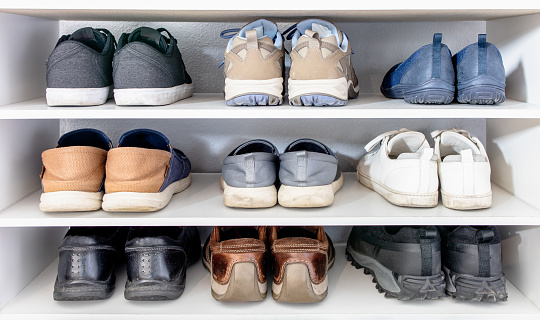 Many shoes of man and woman in different fashion style put in 3 stories white shoe rack. Everyday footwear collection use for variation seasons and lifestyles (sport, casual and leather business shoes).