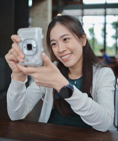 5G internet Asian Gen z Millennial asian women holding instant film cacamera and taking a photo with friend for upload in social media