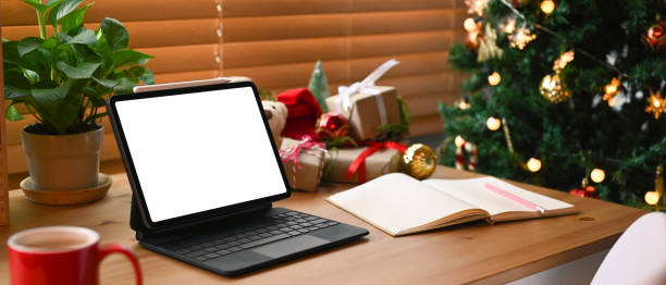 istock Digital tablet with blank screen and Christmas gift boxes on wooden table. 1345933073