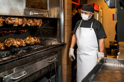 Professional cook looking at a stack of grilled chicken on a skewer in the grill in a restaurant.