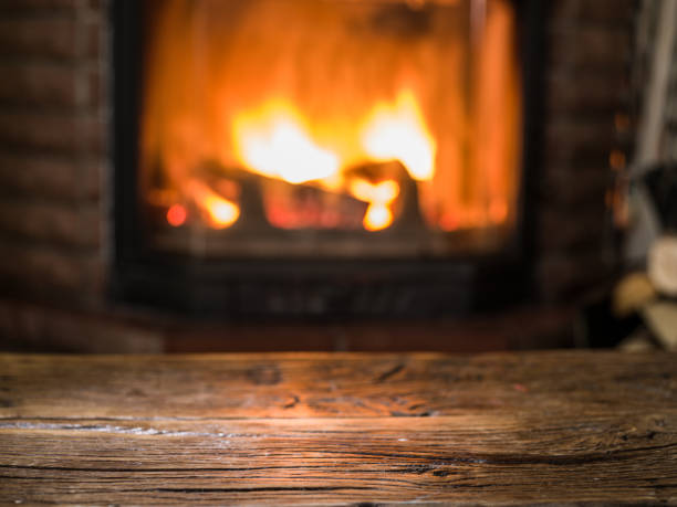 istock Old wooden empty table and  blurred burning fire in fireplace at the background. Empty tabletop can be used as mock up for photo design. 1345935573