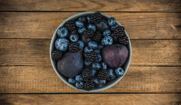 Dark berries and fruits in the bowl on the rustic background. Shot from above. Selective focus.