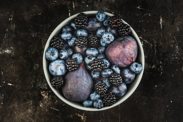 Dark berries and fruits in the bowl on the rustic background. Shot from above. Selective focus.