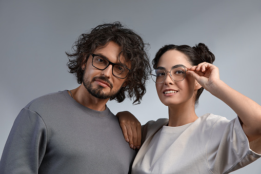 Eyewear concept. Portrait of gorgeous fashion couple in casuale clothes wearing trendy glasses and posing over gray background together. Perfect skin. Vogue style. Close up. Studio shot