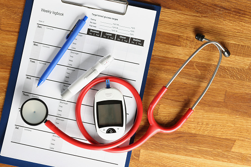 Glucometer with stethoscope lying on glucose control document closeup. Diabetes treatment concept