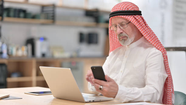 istock Old Arab Businessman Working on Laptop and Smartphone at Work 1345939902