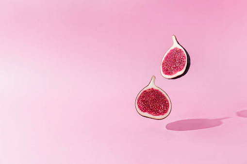 Fresh tasty fig fruit halves levitation with shadow on pink background. Two cross sections of fig falling down or fly. Vegan desert concept. Shadow of flying healthy eating food. High quality photo