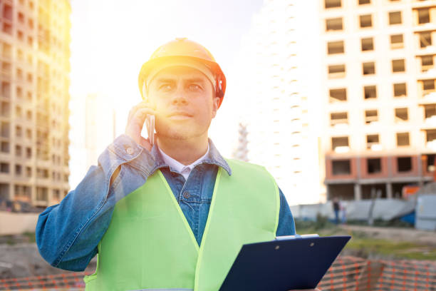 istock Engineer in red protective helmet with blueprint use smartphone at construction site 1345945790