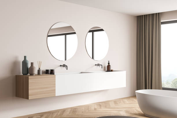 istock Modern bathroom vanity with two round mirrors on beige wall. Corner view. 1345947572