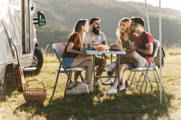 istock Young cheerful couples talking at picnic table by the camp trailer. 1345949947
