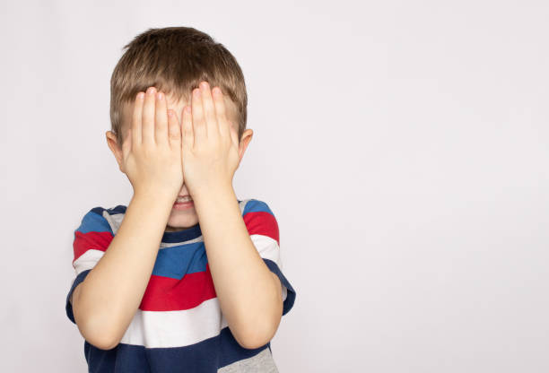 istock Cute little boy kid covering his face with hands against gray background 1345950372