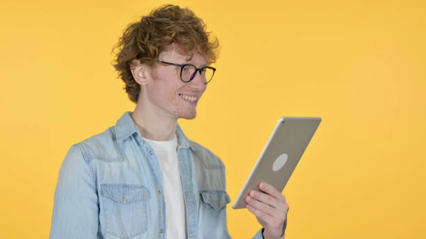 istock Video Call on Tablet by Redhead Young Man on Yellow Background 1345950406