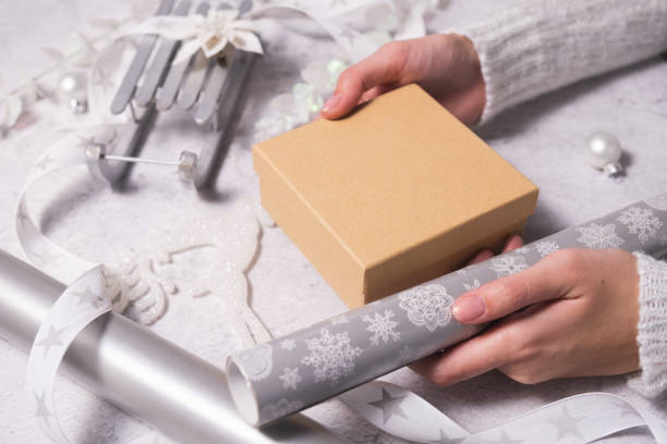 istock Female hands hold gift box for packaging in silver and white for Christmas. Mockup 1345953874