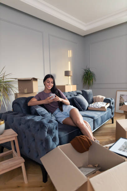 istock Relaxed woman using smart phone on sofa at her new apartment. 1345957357