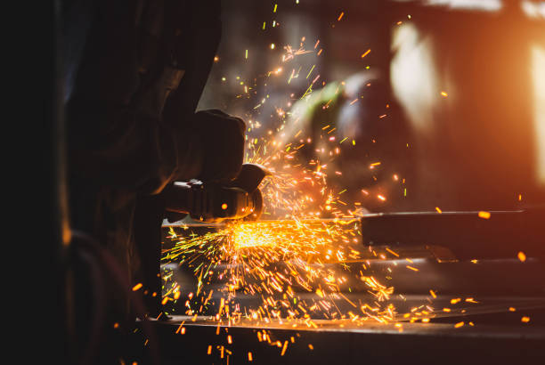 istock A man grinds metal. In the background a welder welds a part. 1345961749