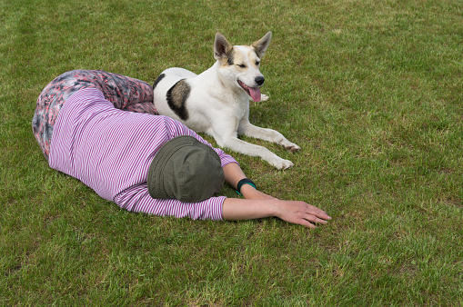 Mature Caucasian woman and  young white mixed breed dog lying next to each other on a cut lawn at summer season