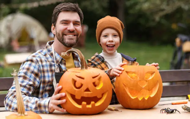 Photo of Smiling father and little boy son carving pumpkins in backyard