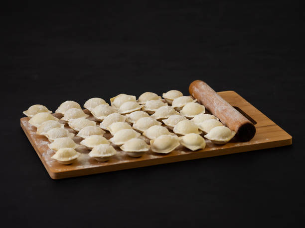 istock Raw Russian dumplings on a cutting board. Homemade dumplings on a black background. The process of preparing meat dumplings, ravioli. 1345964285