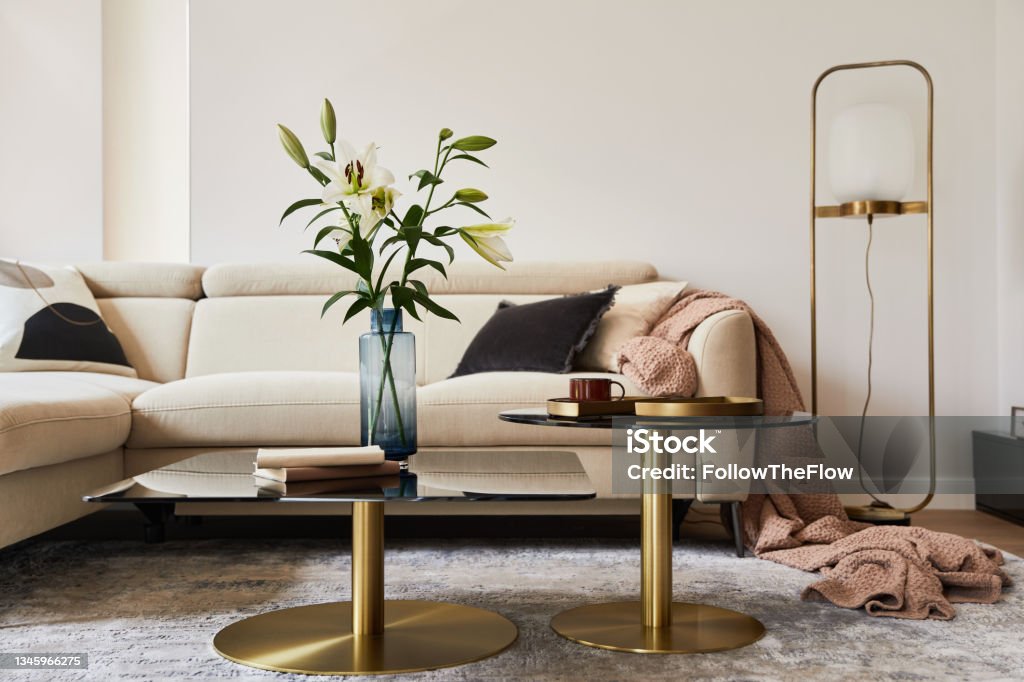 Stylish living room interior composition with beige sofa, glass coffee table, carpet on the floor and glamorous accessories. Template. Gold Colored Stock Photo
