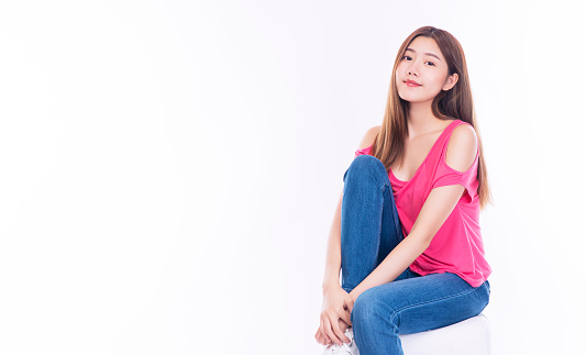 Joyful young woman with long hair wear pink t-shirt showing palm hand while sitting on chair over isolated against white background.