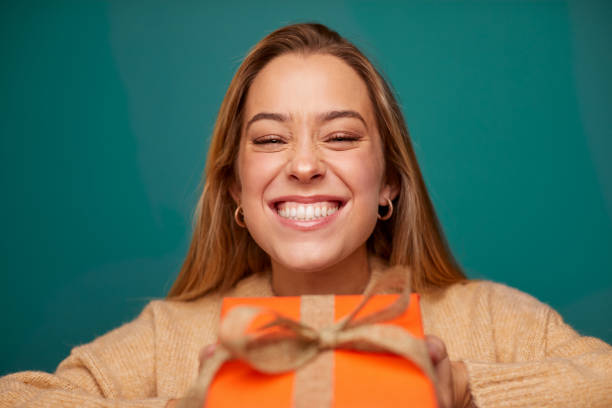 istock A young beautiful woman grinning behind a Christmas gift. 1345967023