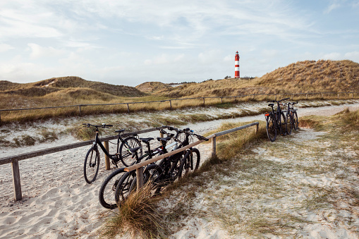 Various bicycles leaning on wooden stands at bike parking place. Red and white striped lighthouse in background. Summer vacation, holiday at sea concept.