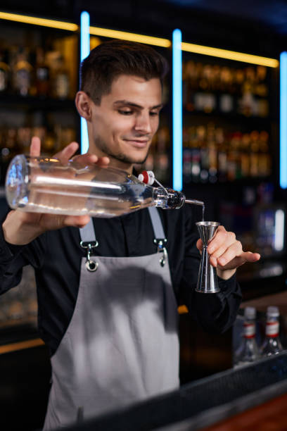 istock Bartender in apron adds ingredient to glass 1345968128