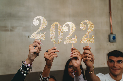 Detail of four hands holding a glitter 2022 number. New year's eve 2022 concept.