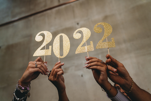 Detail of four hands holding a glitter 2022 number. New year's eve 2022 concept.