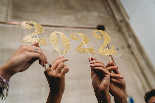 Detail of four hands holding a glitter 2022 number. New year's eve 2022 concept.