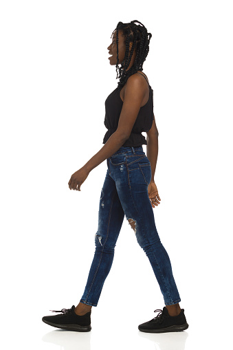 Black woman in casual clothes is walking and talking. Side view. Full length studio shot isolated on white.