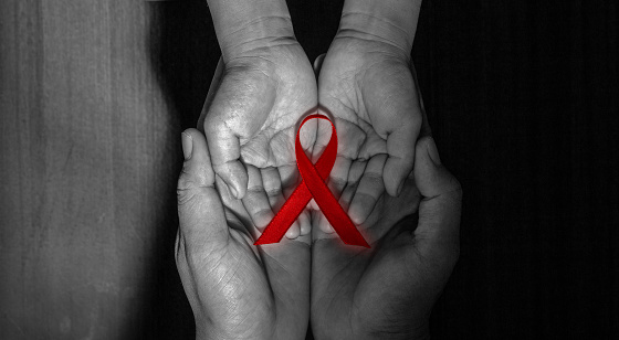 a red ribbon on child's hands held by adult's hands on world aids day.