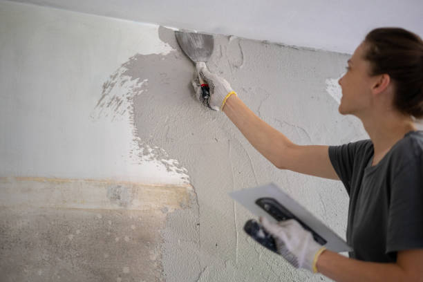 istock Young woman doing home repairs by applying plaster on the wall using a trowel 1345971598