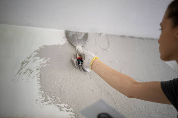 istock Young woman doing home repairs by applying plaster on the wall using a trowel 1345971698