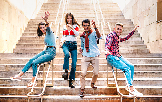 Multiethnic friends walking down stairs with stupid funny moves - Happy guys and girls having fun at urban city center on party mood - College students in travel holidays  - Bright warm filter