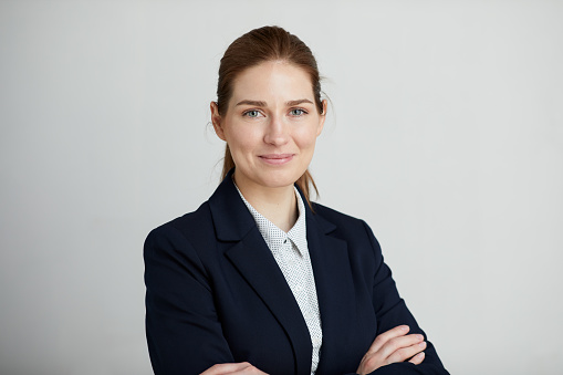 A professional black businesswoman in a blue blazer stands with arms crossed in a modern office, exuding confidence and leadership.