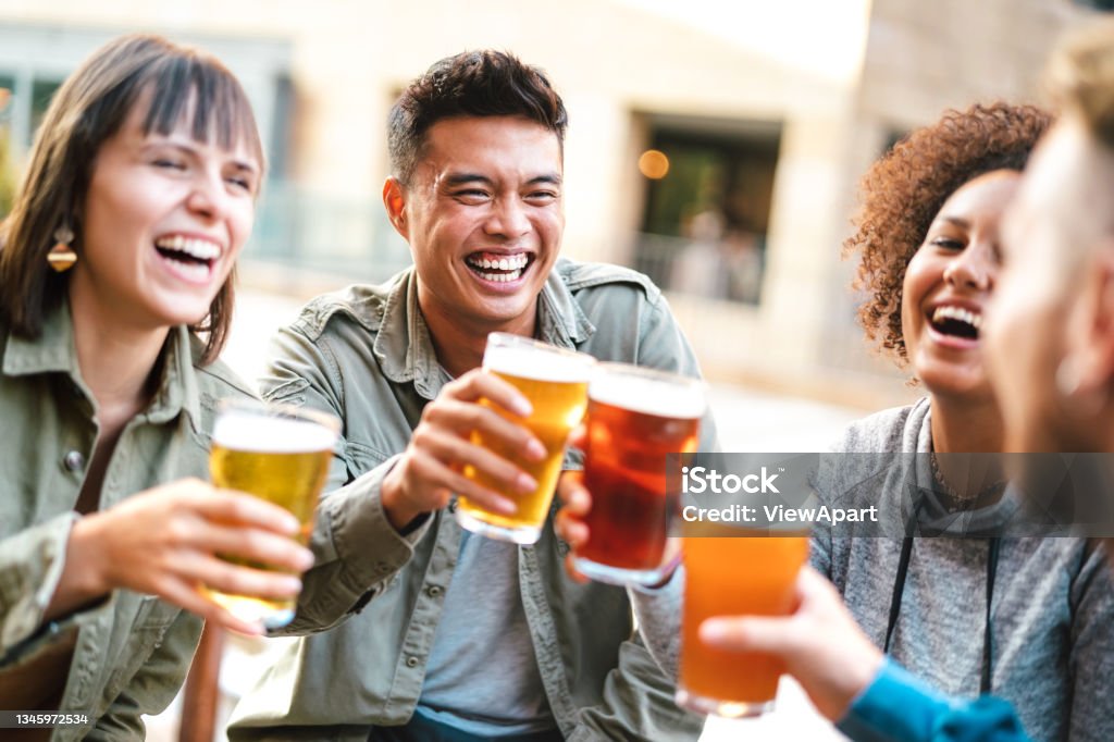 Group of happy multiethnic friends drinking and toasting beer at brewery bar restaurant - Beverage concept with men and women having fun together outside Brewery Stock Photo