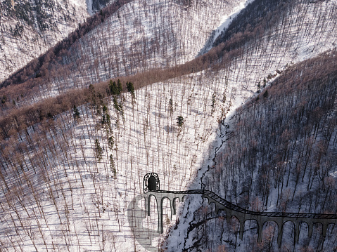 High angle view of a snow-covered winter the mountains with a drawing of a road and a tunnel in the steep slopes.