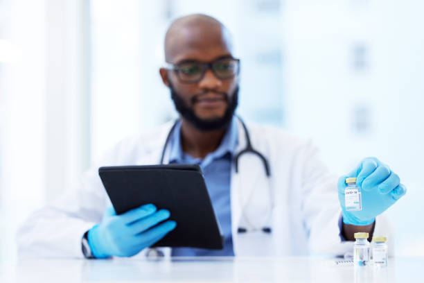 istock Shot of a young doctor sitting in his clinic and using a digital tablet while checking Covid-19 vaccine vials 1345974936