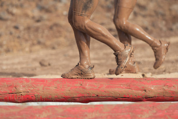 Mud race runners. Participants walking on the tree trunk, catches balance above the pit full of water
