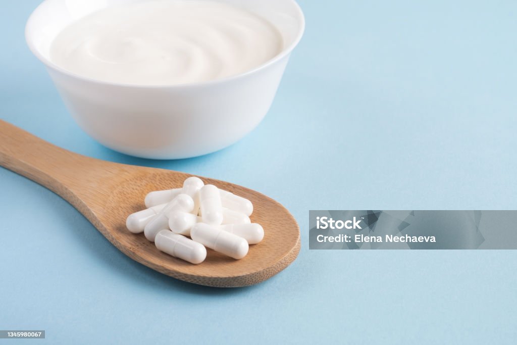 Fermented foods, dairy, nutritional supplement. Homemade yogurt with probiotics and capsules pills on a wooden spoon. Close up, copy space Probiotic Stock Photo