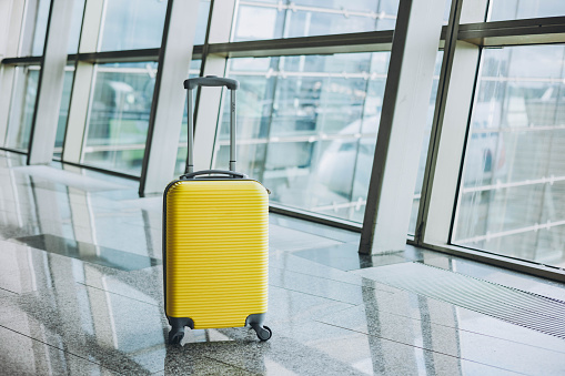 Yellow suitcase in airport departure lounge on airplane background. Travel and summer vacation concept. Bright suitcase in airport terminal waiting area.