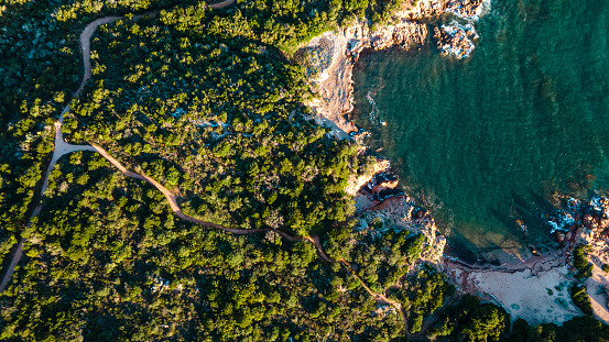 early in the morning, sunrise on an island in the mediterranean sea. warm light, paths leading to the bay, many green bushes and plants. soft blue water, waves breaking in the reef. drone, aerial view