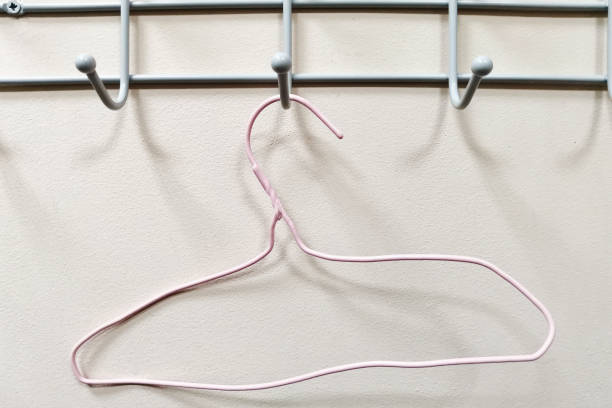 Pink curved old clothes hanger hanging on a hook against an empty wall background